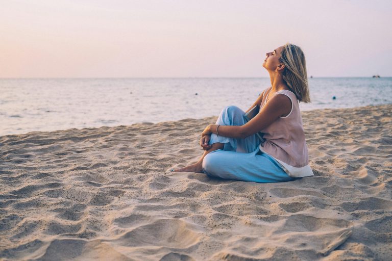 A peaceful moment as a woman relaxes on a sandy beach, enjoying the sunset.